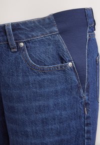 Mørkeblå denimjeans med elastisk taljebånd. Indeholder en forlommer med en sølvnitte. Teksturen er glat med et let falmet mønster.