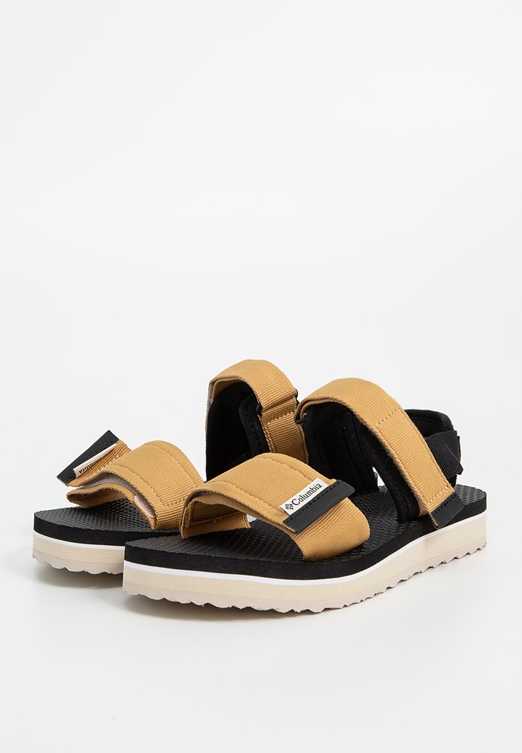 Sandales beige et noires avec des sangles en tissu ajustables, semelle noire texturée et semelle extérieure blanche. Logo de la marque sur la sangle.