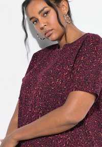 Camicia a maniche corte con stampa leopardo bordeaux, scollatura rotonda e texture in cotone morbido. Presenta macchie scure e un design a vestibilità comoda.