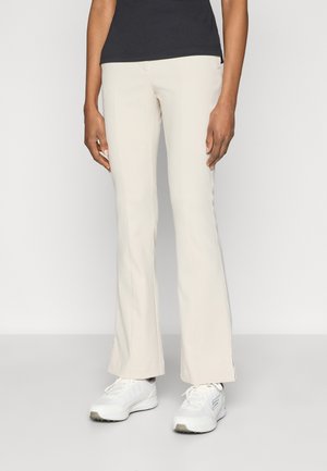 Flarebukser i kremfarge med glatt tekstur, som har en subtil sidesliss og en tilpasset midje, kombinert med hvite treningssko.
