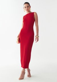 Punane, keha järgiv kleit ühekärast kujundusega, valmistatud siledast kangast. Koos kuldsete aksessuaaride ja nudesandaalidega.