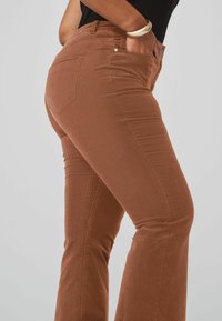 Pantalones marrones acampanados de tela texturizada. Presenta dos bolsillos traseros y detalles de costura a lo largo de las costuras. Cintura plana en la parte delantera.
