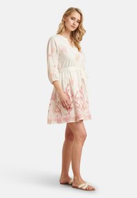 White dress with pink floral patterns, three-quarter sleeves, wrap style, and a tie belt. Lightweight fabric, relaxed fit, knee-length.