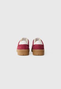 Røde semskede sneakers med hvide læderdetaljer og brune gummisåler. Har en rund form og minimalistisk design med branding på hælen.