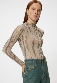 Doorzichtig langmouwen top in beige met bruine verticale strepen, gecombineerd met hoge taille spijkerbroek met een gestructureerde blauwe afwerking.