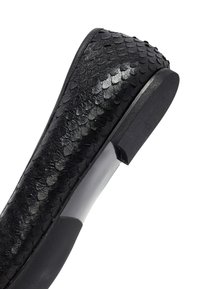 Zapato plano negro con un upper de cuero texturizado, similar a escamas, puntera redondeada, suela de goma y un tacón bajo, ligeramente curvado.