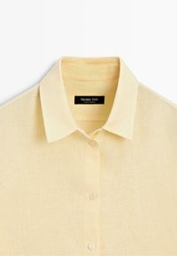 Chemise en lin jaune clair avec boutons, col pointu et étiquette de marque noire indiquant « Massimo Dutti » à l'intérieur du col.