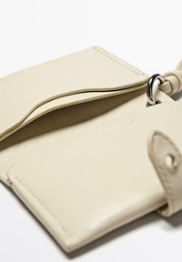 Beige leather wallet with a textured finish, featuring a central fold, metal hardware ring, and smooth interior pockets.