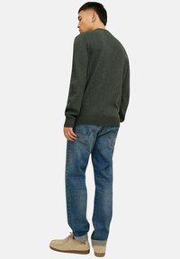 Dunkelgrüner Strickpullover mit gerippten Bündchen, kombiniert mit hellblauen geraden Jeans und beigen Schnürschuhen. Glatte Textur und lässige Passform.