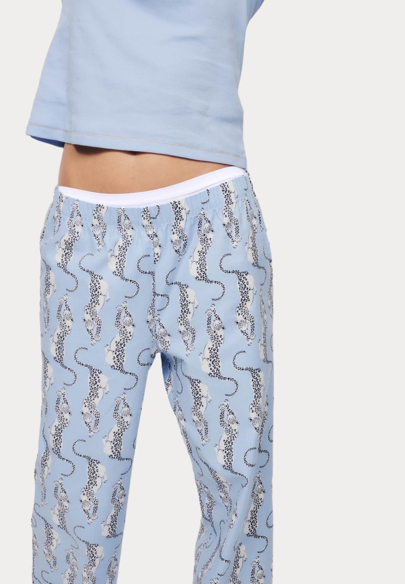 Pantalons de pyjama bleu clair avec un motif léopard noir et blanc sur l'ensemble. Dotés d'une taille élastique et d'une coupe ample.