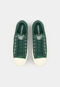 Grønne kanvas sneakers med beige gummisåler, hvit tåhette, sølv øyeskruer og "Converse All Star" merke på tungen.