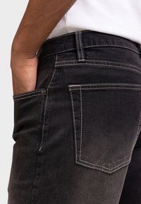 Ξεθωριασμένο μαύρο τζιν με αντίθετες λευκές ραφές, με πίσω τσέπη και πλαϊνή τσέπη, εμφανιζόμενο σε άτομο που φοράει λευκό τοπ.