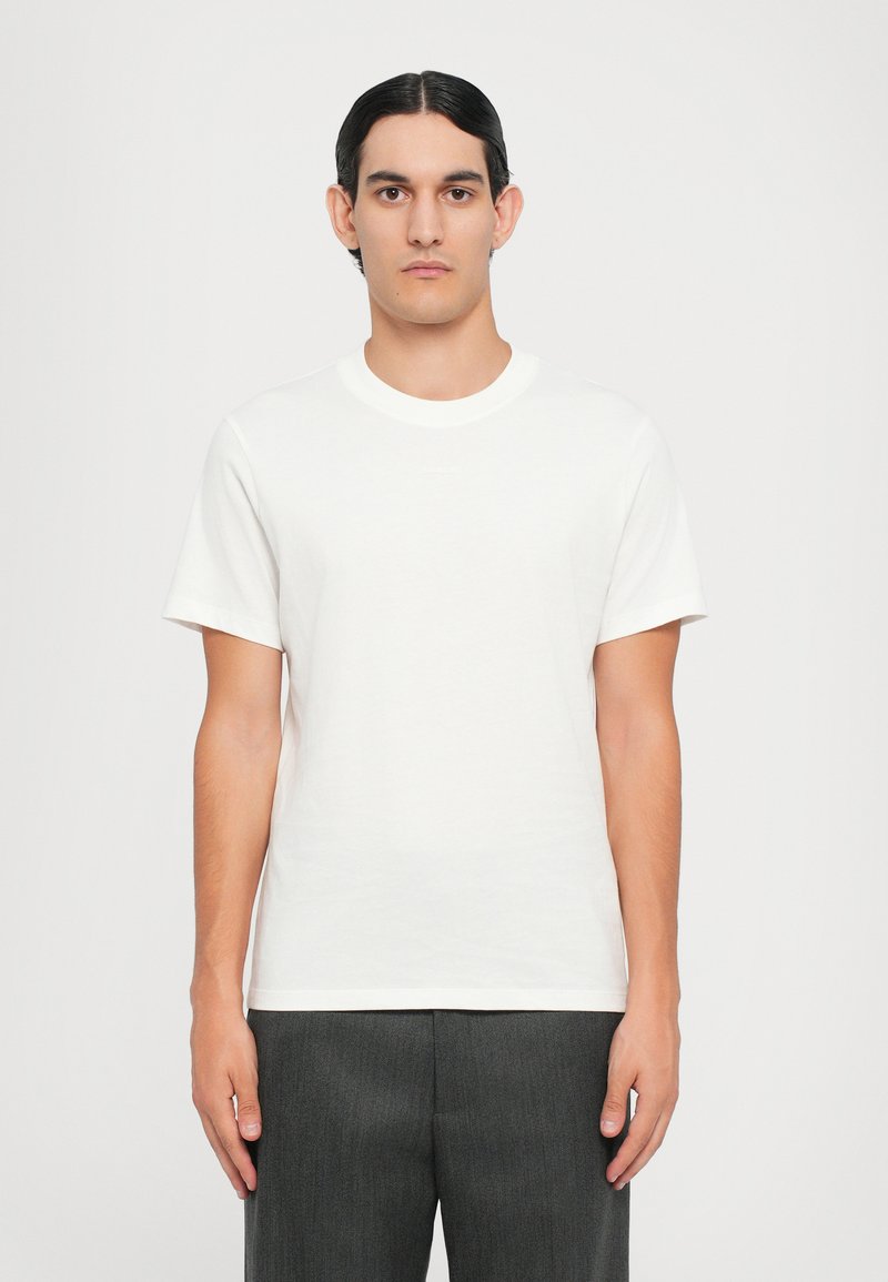 Hvit bomulls t-skjorte med rund hals og korte ermer; glatt tekstur, minimalistisk design og subtil branding på forsiden.