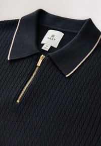 Marineblauw geribd poloshirt met een ritssluiting, voorzien van een contrasterende lichtgekleurde kraag en gouden details. Merkenteken zichtbaar.