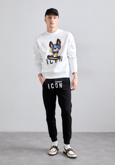 Hvid sweatshirt med farverig grafik og "ICON" tekst, parret med sorte sweatpants med lignende branding og elastisk talje.