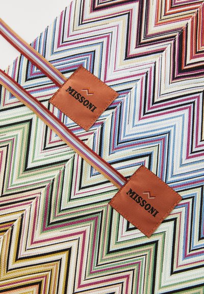 Tkanina s višebojnim cik-cak uzorkom koja sadrži dvije smeđe kožne oznake s utisnutim "MISSONI", prikazujući različite boje i teksture.