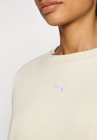 Vaaleanbeige collegemekko, joka on valmistettu pehmeästä kankaasta ja jossa on pyöreä pääntie sekä pieni laventelinvärinen logo rinnassa. Siisti rakenne ja rento muotoilu.