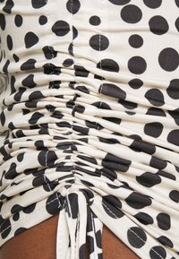 Svart och beige rynkad tyg med ett prickigt mönster, med texturerad sömnad och samlade detaljer på sidan.
