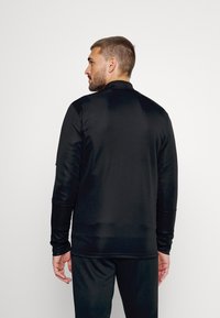 Zwarte atletische langemouwen shirt met een gladde textuur, hoge kraag en aansluitend ontwerp. Achteraanzicht toont slanke lijnen en geen zichtbare patronen.