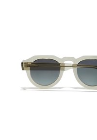 Ümmargused prillid, millel on läbipaistev valge raam, varjundiga gradatsiooniklaasid ja kuldse tooni metallaktsendid templitel.