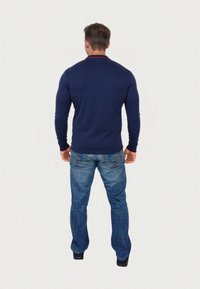 Navy long-sleeve polo with a red collar, paired with light blue denim jeans. The fabric appears textured, and the fit is close to the body.
