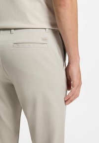 Hellbeige Hose mit glatter Textur, ausgestattet mit Gesäßtaschen und einem kleinen, gebrandeten Patch mit der Aufschrift "BOSS." Schlichter und maßgeschneiderter Schnitt.