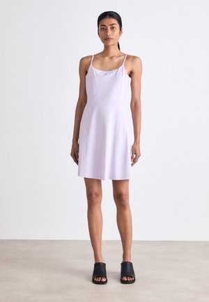 Lilac spaghetti strap dress with a fitted bodice and flared skirt, made of smooth fabric. Worn with black open-toe mules.
