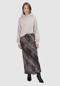 Sweat à capuche beige avec une coupe décontractée et une poche frontale, associé à une longue jupe imprimé léopard aux tons foncés et clairs. Bottines noires.