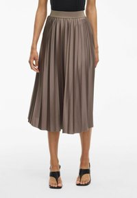 Jupe midi plissée en satin marron avec une taille élastique. Forme évasée avec une texture lisse, associée à des sandales noires à lanières.