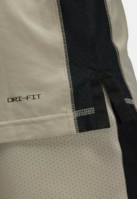 Beige DRI-FIT stof med sorte mesh paneler, der har en glat tekstur og perforeret design. Inkluderer kontrastsyning og stofdetaljer.