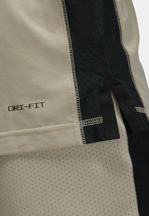 Beige DRI-FIT stof med sorte mesh paneler, der har en glat tekstur og perforeret design. Inkluderer kontrastsyning og stofdetaljer.