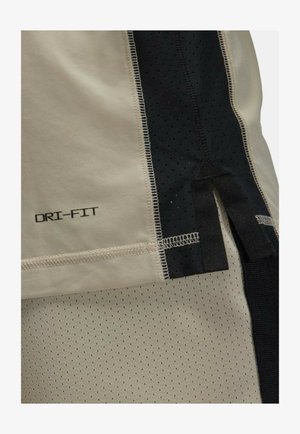 Tejido DRI-FIT beige con paneles de malla negra, que presenta una textura suave y un diseño perforado. Incluye costuras en contraste y acentos de tela.