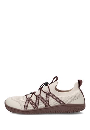 Zapatilla deportiva beige clara sin cordones con elásticos marrones cruzados y suela de goma marrón texturizada, mostrada de perfil.