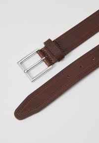 Brown leather belt featuring a polished silver metal buckle, layered stitching, tapered end, and multiple holes for adjustment.