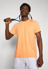 Kurzärmliges, orangefarbiges Sport-T-Shirt aus glattem Stoff. Mit Rundhalsausschnitt, Nahtdetails und einem Logo auf der linken Schulter.
