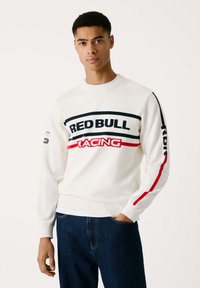 Suéter de crewneck blanco con el texto "RED BULL RACING" en negro y rojo. Mangas largas con rayas de acento rojas. Textura de punto suave.
