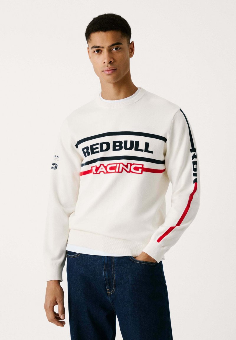 Suéter de crewneck blanco con el texto "RED BULL RACING" en negro y rojo. Mangas largas con rayas de acento rojas. Textura de punto suave.
