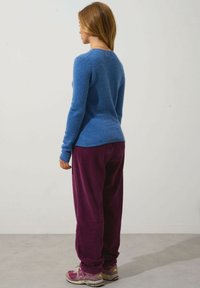 Blauer Langarmpullover aus weichem Material, kombiniert mit lila Cordhosen. Auffällige Details sind die gerippte Textur und die lockere Passform.