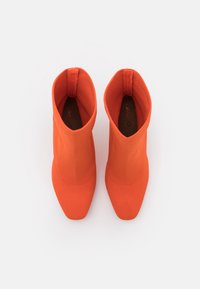 Bottines orange en tissu extensible lisse, avec des pointes pointues et une silhouette épurée. Design minimaliste, sans matériel ni accents visibles.