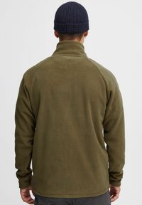 Olivgrüne Fleecejacke mit hohem Kragen, langen Ärmeln und Raglannähten. Der Stoff hat eine weiche, strukturierte Oberfläche.
