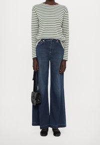 Zeleno-bílé pruhované tričko s dlouhým rukávem, doplněné širokými tmavě modrými džíny. Černá kabelka a černé ploché boty dotvářejí outfit.