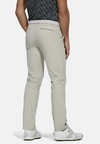 Licht beige golfbroeken met een slim fit, voorzien van achterzakken en een witte geweven riem, gecombineerd met witte sportieve schoenen.