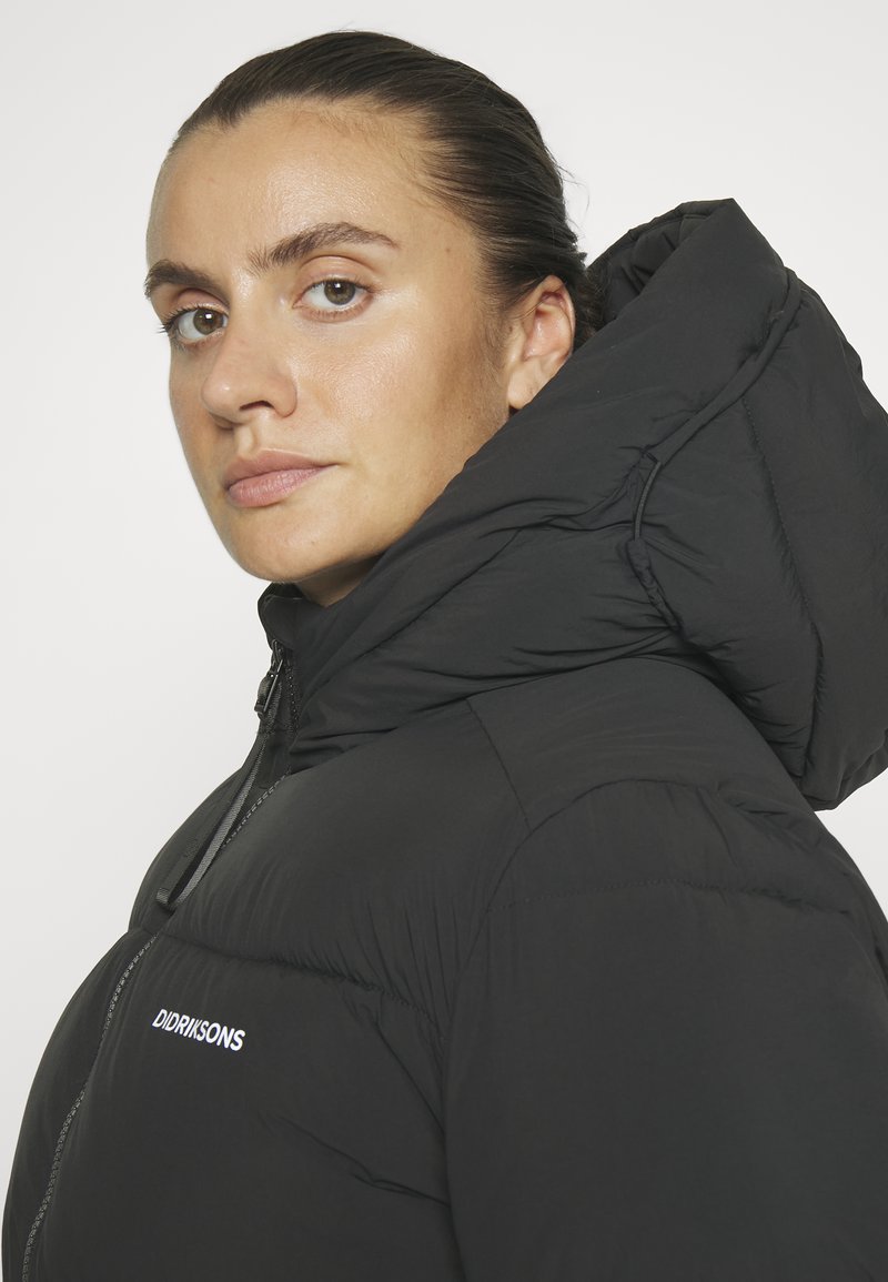 Schwarze Daunenjacke mit hohem Kragen und übergroßer Kapuze, ausgestattet mit einem Reißverschluss und gesticktem Logo auf der linken Seite. Glatte Textur.