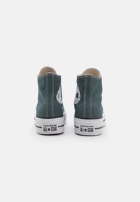 Zelené vysoké tenisky z plátna s kontrastním bílým prošíváním, gumovou podrážkou a kulatou nášivkou s logem na každé straně.