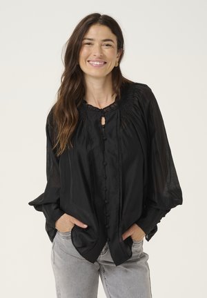 Blusa nera leggera con colletto arricciato, chiusura a bottoni e maniche a campana, abbinata a pantaloni in denim grigi. Tessuto liscio, design fluido.