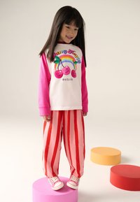 Laste riietus, mis sisaldab valget ja roosat pika varrukaga särki kirsigraafikuga, seda täiendavad punase ja roosa triibuga püksid ning roosad tossud.