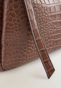 Geantă din piele cu model de crocodil maro, având o suprafață texturată și o bandulieră elegantă, cu detalii de cusătură contrastantă pe margine.