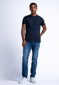 Námořnické tričko s krátkým rukávem s červenými trojúhelníkovými vzory, spárované s modrými džínami a bílými teniskami. Jednoduchý, ležérní design.