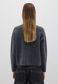 Maglione grigio in lana con vestibilità rilassata, spalle scese e orlo a costine, abbinato a jeans in denim scuri con cuciture a contrasto.
