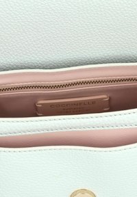 L'interno della borsa in pelle bianca presenta un rivestimento rosa liscio, una tasca con zip e un'etichetta che indica "Coccinelle Pelle Italiana Autentica."